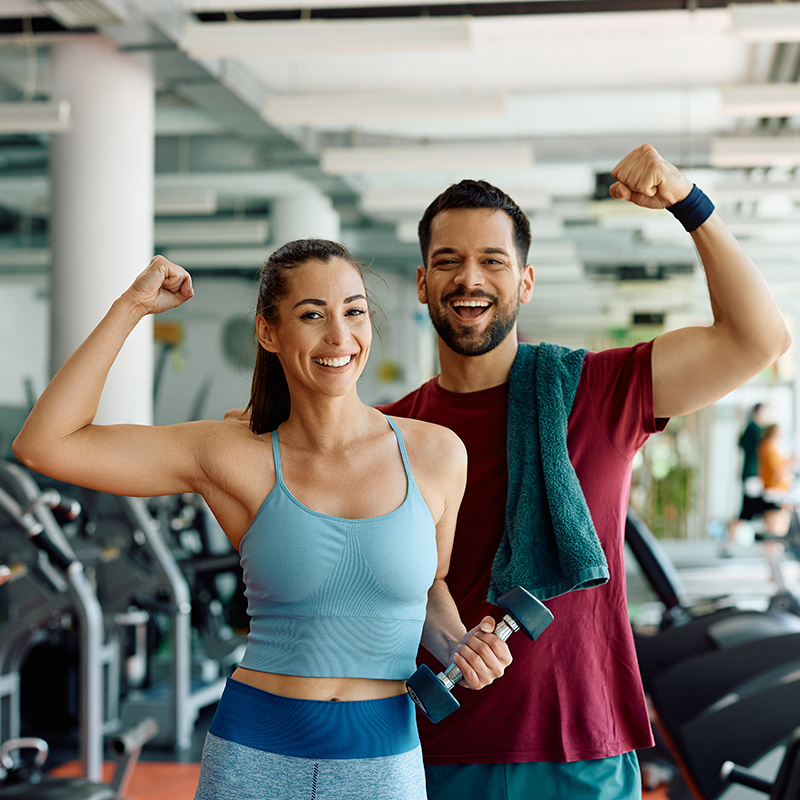 Happy athletic couple flexing their muscles after working out in gym